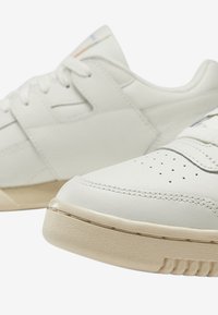 Sneakers bianchi in pelle con una finitura liscia, dotati di punta forata, lacci piatti e suola beige leggermente testurizzata.