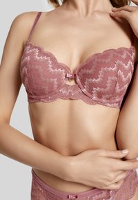 Lace bra in soft rose color with zigzag pattern, scalloped edges, push-up design, and small central bow detail. Adjustable straps.