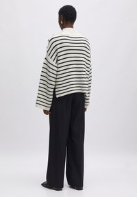 Gestreifter Strickpullover in Creme und Schwarz mit lockerer Passform, breiten Ärmeln und einem gerippten Kragen. Kombiniert mit schwarzen weiten Hosen.
