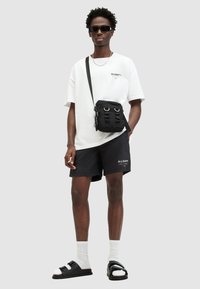 Black crossbody bag with straps, white oversized t-shirt, black shorts with logo, black sandals with buckles, white socks.