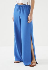 Blauwe wijde broek met een elastische taille en zijsplitten. Glad, lichtgewicht stof. Combinatie met bruine platte sandalen.