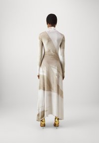 Lang, aansluitend jurkje in crème en beige, met abstracte patronen. Zachte, gladde textuur; heeft lange mouwen en een hoge halslijn. Gouden hakken zichtbaar.