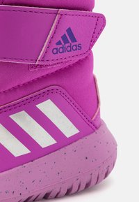 Růžová sportovní bota s textilním svrškem, vybavená bílým designem tří pruhů, texturovanými akcenty a flekatou gumovou podrážkou.