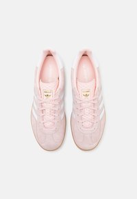 Sneakers in suede rosa chiaro con dettagli in pelle bianca, tre strisce bianche e una linguetta testurizzata con un logo dorato. Suola in gomma color miele.