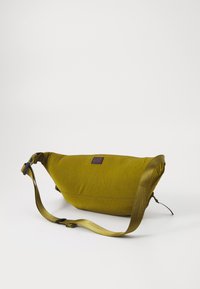Green fabric shoulder bag with a curved design, adjustable strap, and a small logo patch. Smooth texture with no visible patterns.