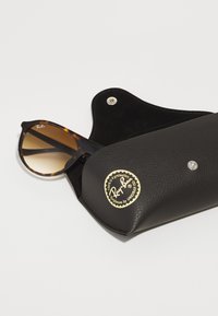 Ochelari de soare Ray-Ban cu rame din plastic brocat și lentile cu degradé, însoțiți de o etui din piele neagră cu logo embosat aurit și închidere tip snap.