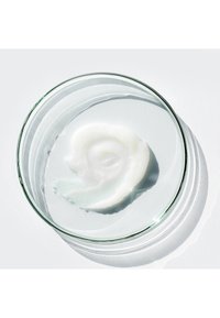 En klar glasfat som innehåller en spiralformad, glänsande, vit geléliknande substans med en lätt strukturerad yta, placerad mot en ljus bakgrund.