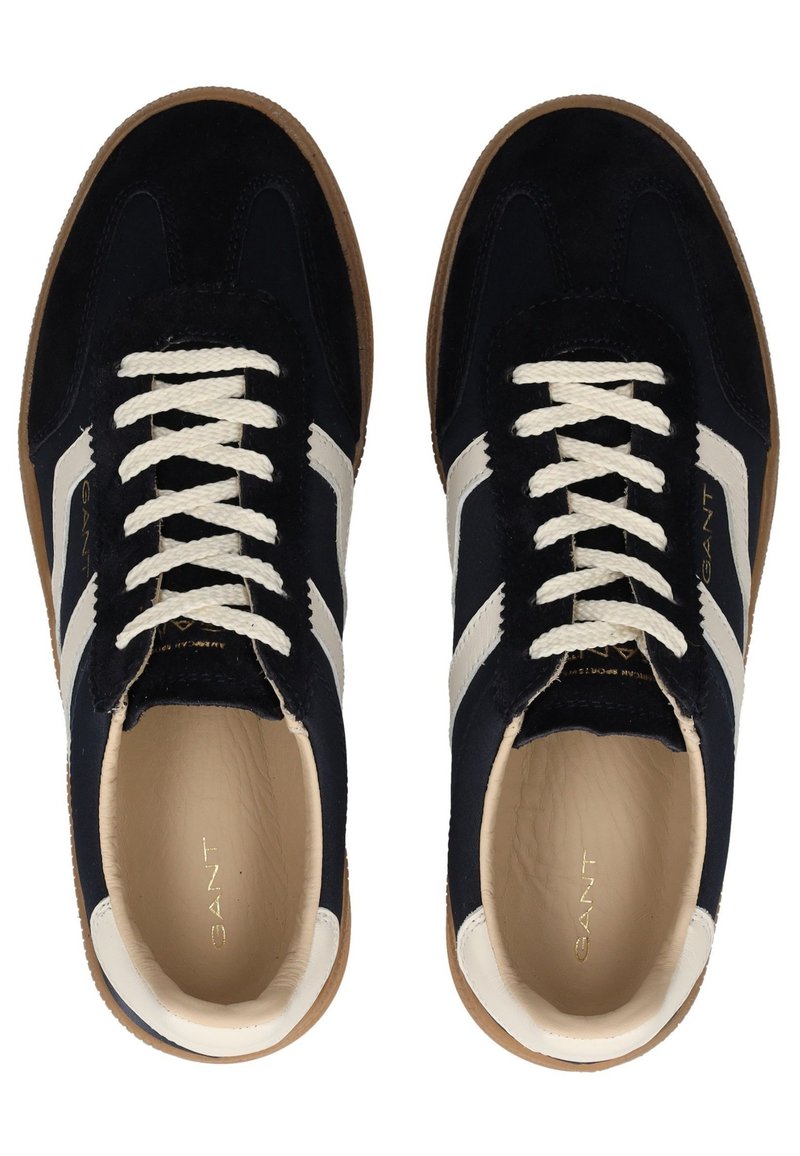 Granatowe zamszowe trampki z białymi skórzanymi paskami, kremowymi sznurowadłami i brązową gumową podeszwą. Wewnątrz znajdują się wytłoczone logo 'GANT'.