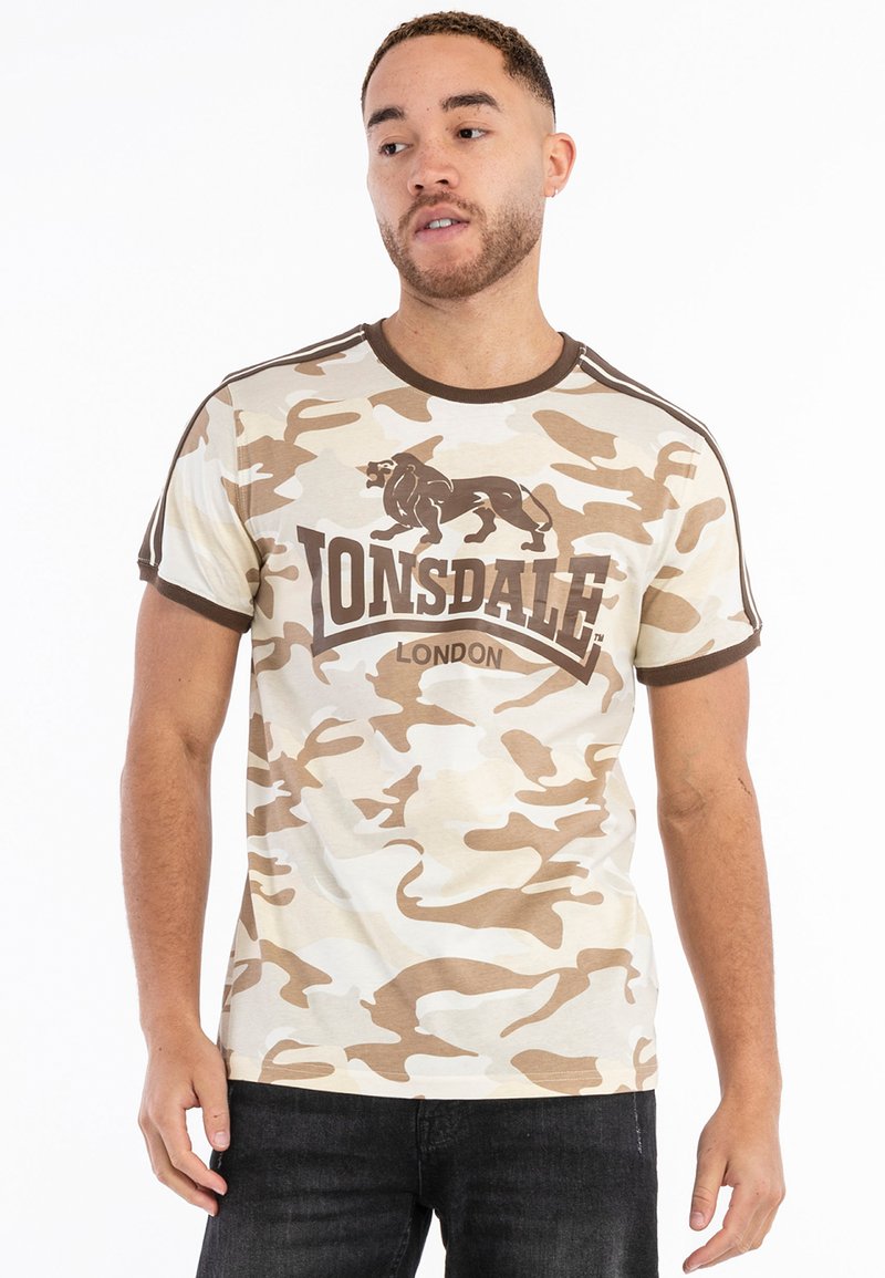 Beige kamufláž tričko s tmavo hnedými akcentmi, so zobrazením leva a logom Lonsdale. Krátke rukávy a dizajn s okrúhlym výstrihom.