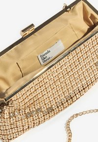 Bolso de mano con un exterior metálico dorado que presenta lentejuelas y rhinestones. El interior está forrado en tela dorada, con una etiqueta que dice "amigos como estos..."