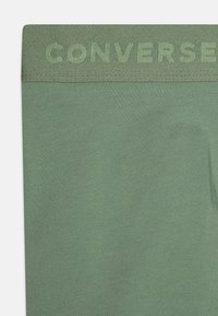 Zelene pamučne tajice s teksturiranim pojasom na kojem je izvezen natpis "CONVERSE" u odgovarajućoj nijansi, prikazujući glatki, prilagođeni dizajn.