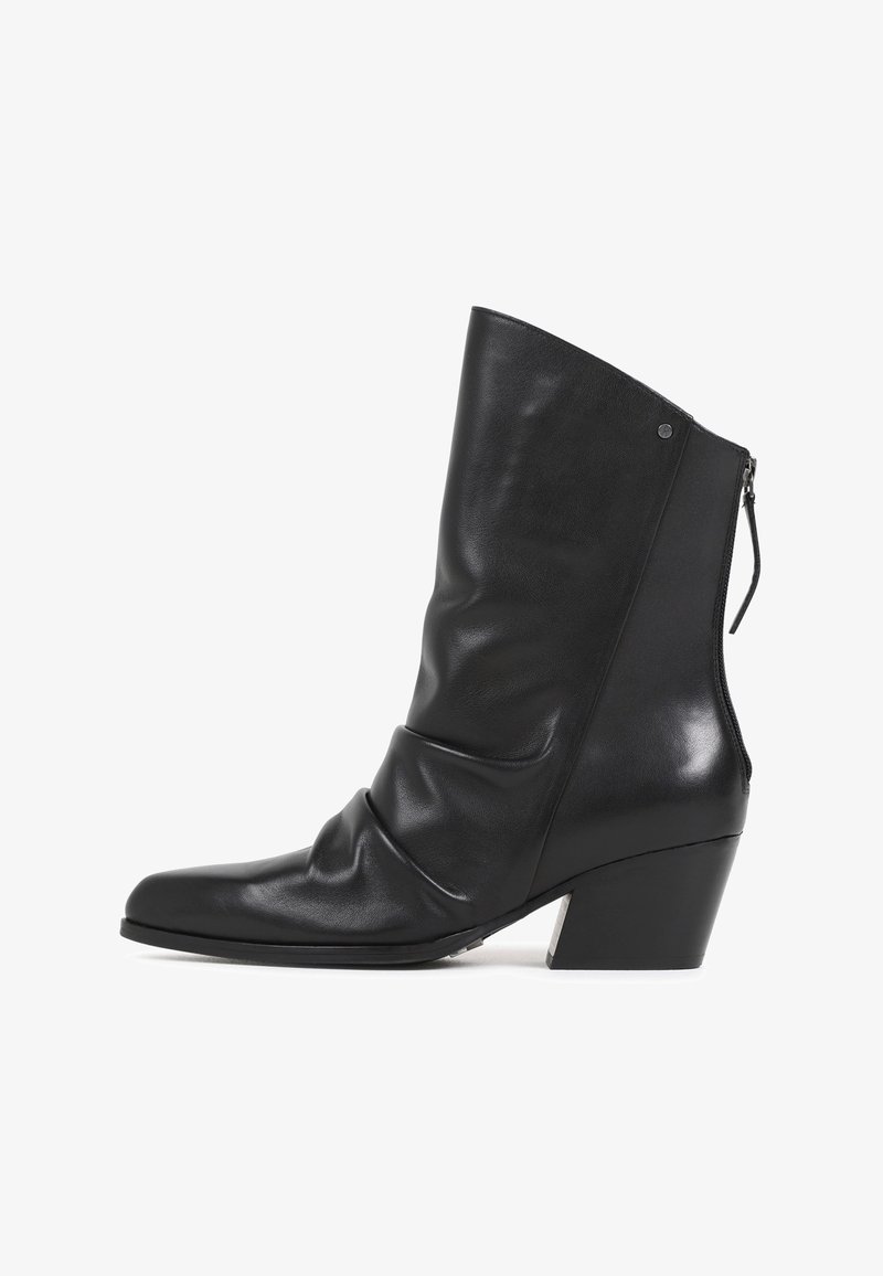 Bottine en cuir noir avec un talon épais de hauteur moyenne et une fermeture éclair à l'arrière, présentant une tige légèrement froissée et un bout rond.
