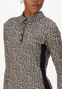 Bluse im Leopardenmuster mit Kragen, Knopfleiste und schwarzen Seitenpaneelen. Hergestellt aus leichtem Stoff mit glatter Textur.