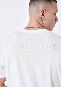 Camiseta de algodón blanca con texto en relieve en color pálido: "PROJECT X PARIS," "MEMBERS' CLUB," y "DISEÑANDO STREETWEAR desde 2015."