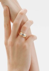 Anillo de oro y plata que presenta dos elementos enlazados en un diseño moderno. El anillo tiene un acabado suave con texturas contrastantes entre los metales.