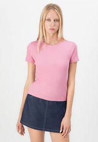 Rosa ribbestrikket t-skjorte med korte ermer og rund hals, kombinert med en mørk denimskjørt med hvite sømmer og en utsvingt fasong.