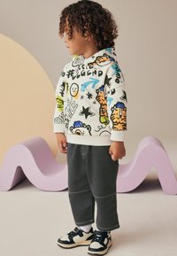 Hættetrøje med multicolorede tegneseriegrafikker, parret med grå sweatpants og sorte sneakers, med hvide detaljer og snørebånd.