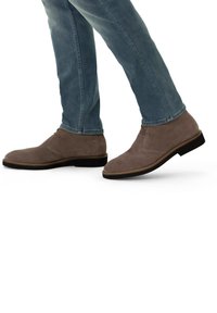 Stivaletti alla caviglia in suede grigio con punta rotonda e tacco piatto, caratterizzati da cuciture minime e una chiusura con lacci. Indossati con jeans blu chiaro.