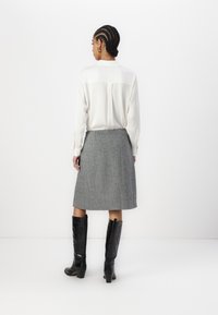 Blusa branca de mangas longas, saia lápis cinza em lã e botas altas pretas com acabamento texturizado. Design simples e ajustado.