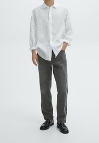 Witte linnen blouse met lange mouwen, gecombineerd met donkergrijze jeans en zwarte instappers. Eenvoudig ontwerp en ontspannen pasvorm.