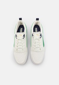 Weiße Sneakers mit grünen Akzenten und perforiertem Zehenbereich, ausgestattet mit flachen Schnürsenkeln und einem marineblauen Innenbereich. Puma-Logo in Gold an der Seite.