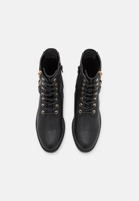 Czarne skórzane botki za kostkę z złotymi akcentami. W skład cech wchodzą sznurowadła oraz zamek błyskawiczny z boku, gładka faktura i zaokrąglony kształt noska.