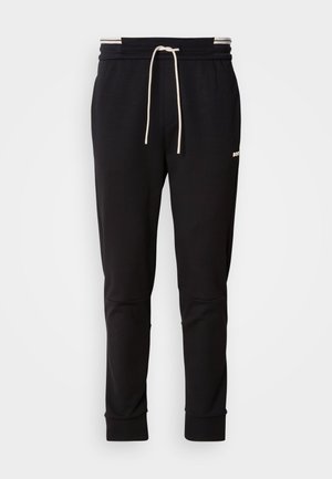 Sorte slim-fit joggebukser med hvit snor, ribbede mansjetter og subtil logo på den øvre låret mot en ensfarget bakgrunn.