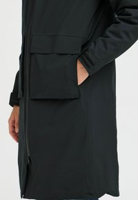 Black parka jacket featuring a zipper closure, two front pockets, and velcro accents on the cuffs for adjustable fit. Smooth, matte texture.