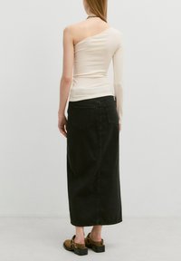 Romige geribbelde top met één schouder, gecombineerd met een lange zwarte denimrok. Tan sandalen met zwarte blokhakken maken de outfit compleet.