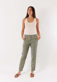 Canotta beige chiaro, pantaloni verdi oliva su misura con tasche laterali e chiusura a bottone, e sandali marroni con design a fascia.