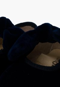 Marineblauwe fluwelen balletschoenen met een gestructureerde afwerking, voorzien van een opvallende strikaccent aan de voorkant en een beige binnenzool.