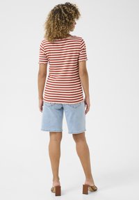 Rood-wit gestreepte ribbenshirt met golvende mouwen, gecombineerd met lichte denimshorts en bruine sandaaltjes met blokhak.