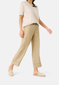 Beige linne vida byxor med uppvikta fållar, ihop med en ljusbeige kortärmad topp och slip-on espadrillos.