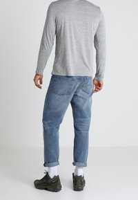 Maglietta grigia a maniche lunghe, jeans in denim blu larghi, con risvolto alle caviglie, calzini bianchi e scarpe da ginnastica verde scuro. Nessun motivo o dettaglio. 