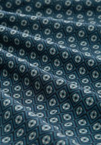 Tissu à motifs en bleu foncé avec des formes géométriques en losange en crème et bleu clair. Texture lisse avec une apparence tissée.