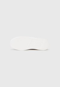 White sneaker outsole featuring a textured surface with a herringbone pattern, smooth rounded toe, and distinct traction grooves.