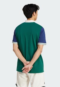 Green and navy short-sleeve polo shirt with white accents; textured fabric; classic collar; back view shows smooth lines and relaxed fit.