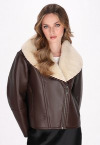 Giubbotto di pelle marrone con un ampio colletto in shearling crema, chiusura con zip e tasche laterali. Il design presenta una silhouette leggermente strutturata.