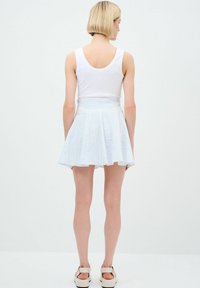 Top bianco in cotone abbinato a una gonna a campana a righe blu e bianche, con pieghe e vita aderente. Indossato con sandali di colore chiaro.