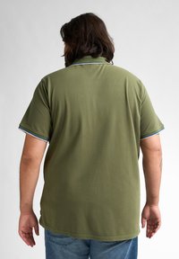 Oliwkowa koszulka polo z krótkimi rękawami, z niebieskimi i białymi paskami na kołnierzyku. Miękka, gładka faktura, swobodny krój.