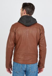 Ruskea nahkatakki harmaan hupparin kanssa. Omistaa sileän pinnan, rento leikkaus, näkyvät tikkaukset ja napilliset hihansuut.