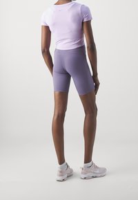 Shorts sportivi viola a vestibilità aderente, abbinati a una maglietta a maniche corte dello stesso colore. Indossati con sneakers rosa chiaro e calzini bianchi.