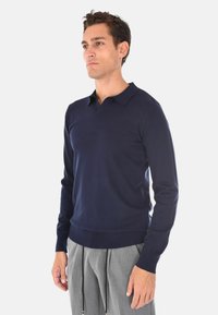 Pullover blu navy a maniche lunghe con colletto polo, realizzato in un tessuto a maglia liscio. Presenta un design aderente e dettagli a coste nei polsini e nell'orlo.
