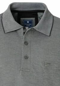 Graues Poloshirt aus strukturiertem Stoff, mit einer Knopfleiste mit drei Knöpfen und einer Brusttasche, die mit einem kleinen Etikett versehen ist. Kontrastierendes Kragenbesatzdetail.