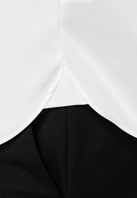 Witte shirtzoom met een gekeerde rand, gelaagd over een zwarte stof eronder. Soepele textuur met zichtbare stikdetails.