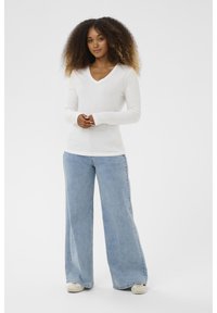 Weißes longsleeve V-Ausschnitt Oberteil kombiniert mit hellblauen weit geschnittenen Jeans. Der Stoff wirkt glatt und leicht, mit einem lockeren Sitz.