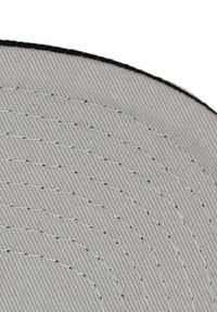 Gros plan sur un tissu gris clair avec des lignes de couture concentriques et une fine bordure noire.