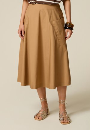Mujer con una falda midi color beige con grandes bolsillos delanteros, una camiseta de rayas, pulseras de carey y negras, y sandalias tejidas con cordones.