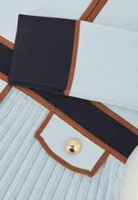 Pletený sveter s pruhmi v svetlomodrej, námorníckej modrej a hnedej farbe, s rebrovanou textúrou a zlatým gombíkom na vrecku.