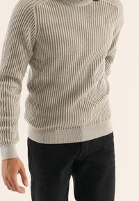 Jasnoszary prążkowany sweter z dzianiny z okrągłym dekoltem i długimi rękawami, wyposażony w elastyczny dół i mankiety, zestawiony z czarnymi dżinsami.